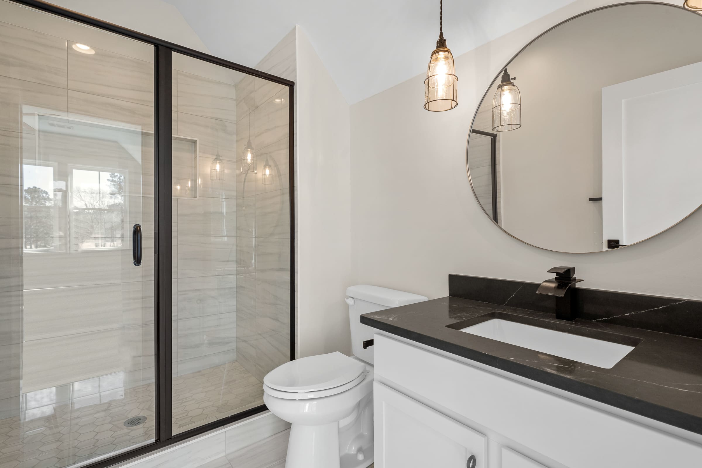 Guest Bathroom with Large Circle Mirror Above Dark Stone Counter Top and White Cabinetry |PAXISgroup